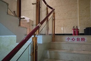A staircase with a wooden handrail, a sign with Chinese characters, and a fire extinguisher on the landing.