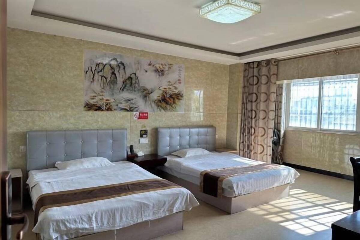 A hotel room with two beds, a large wall painting, a window with curtains, and a ceiling light fixture.