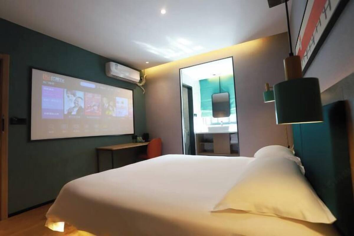 Hotelkamer met een bed, bureau, stoel, televisiescherm en een badkamer die door een open deur zichtbaar is.