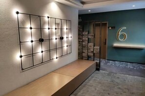 Een receptiegedeelte met een wandlamp, een bank en een deur met het nummer 6.