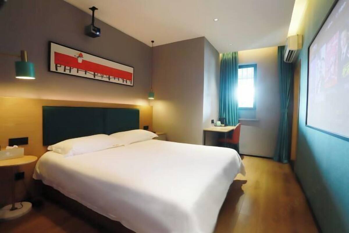 Een hotelkamer met een bed, nachtkastje, bureau met stoel, raam met gordijnen en een wanddecoratie.