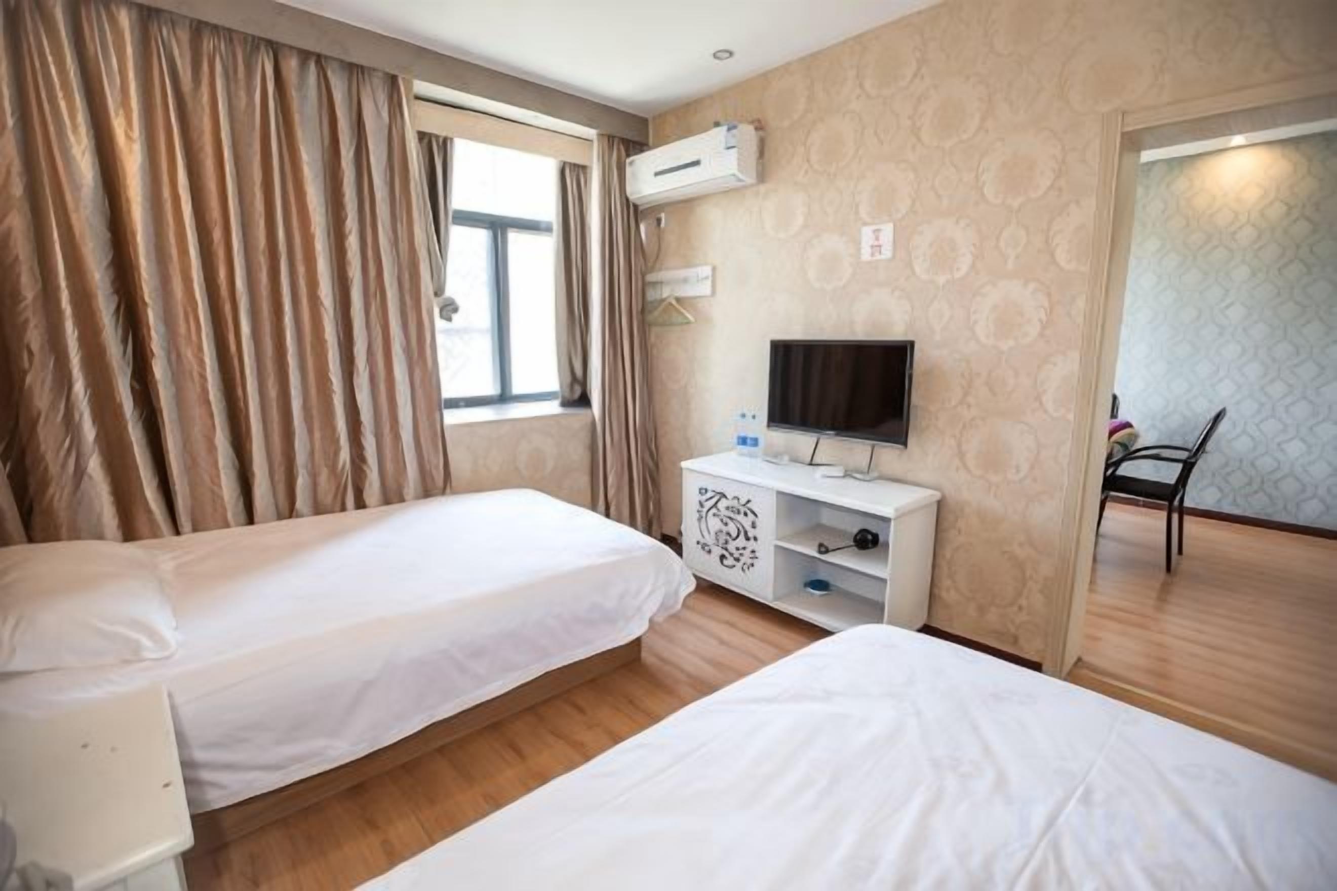 A hotel room with two beds, a TV, a desk with a computer, and a window with curtains.