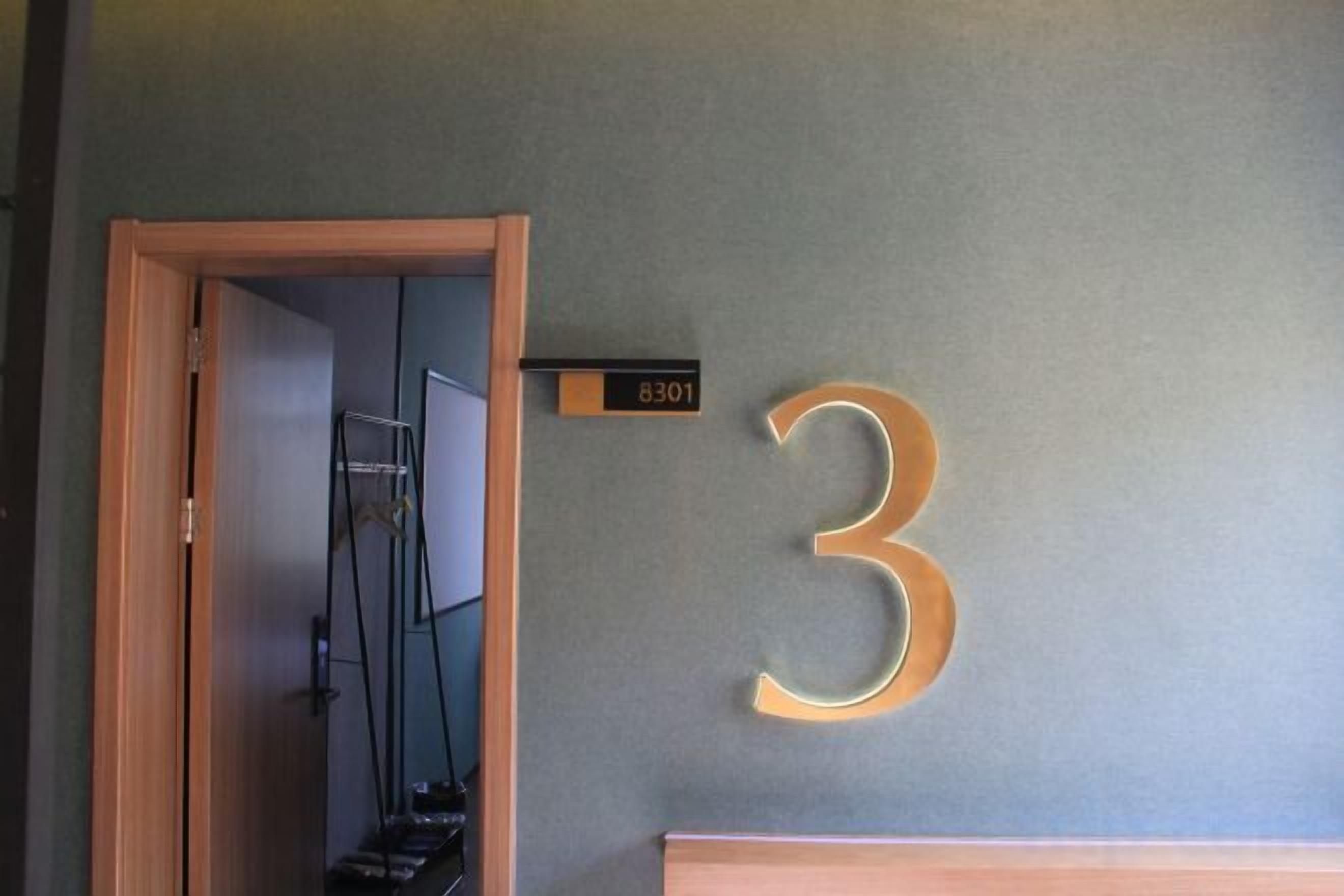 Una habitación con una puerta que da a un pasillo, el número '3' en la pared y un cartel con el número '8301'.