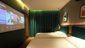 Une chambre d’hôtel avec un lit, un écran de télévision diffusant une émission, un rideau vert et un tableau encadré au mur.