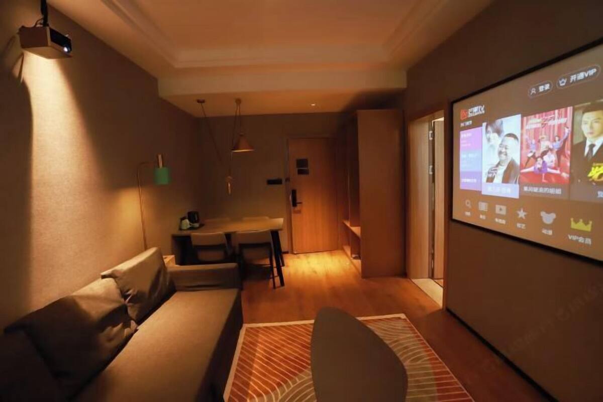 Een moderne woonkamer met een bank, een eethoek en een groot scherm waarop iets wordt afgespeeld.