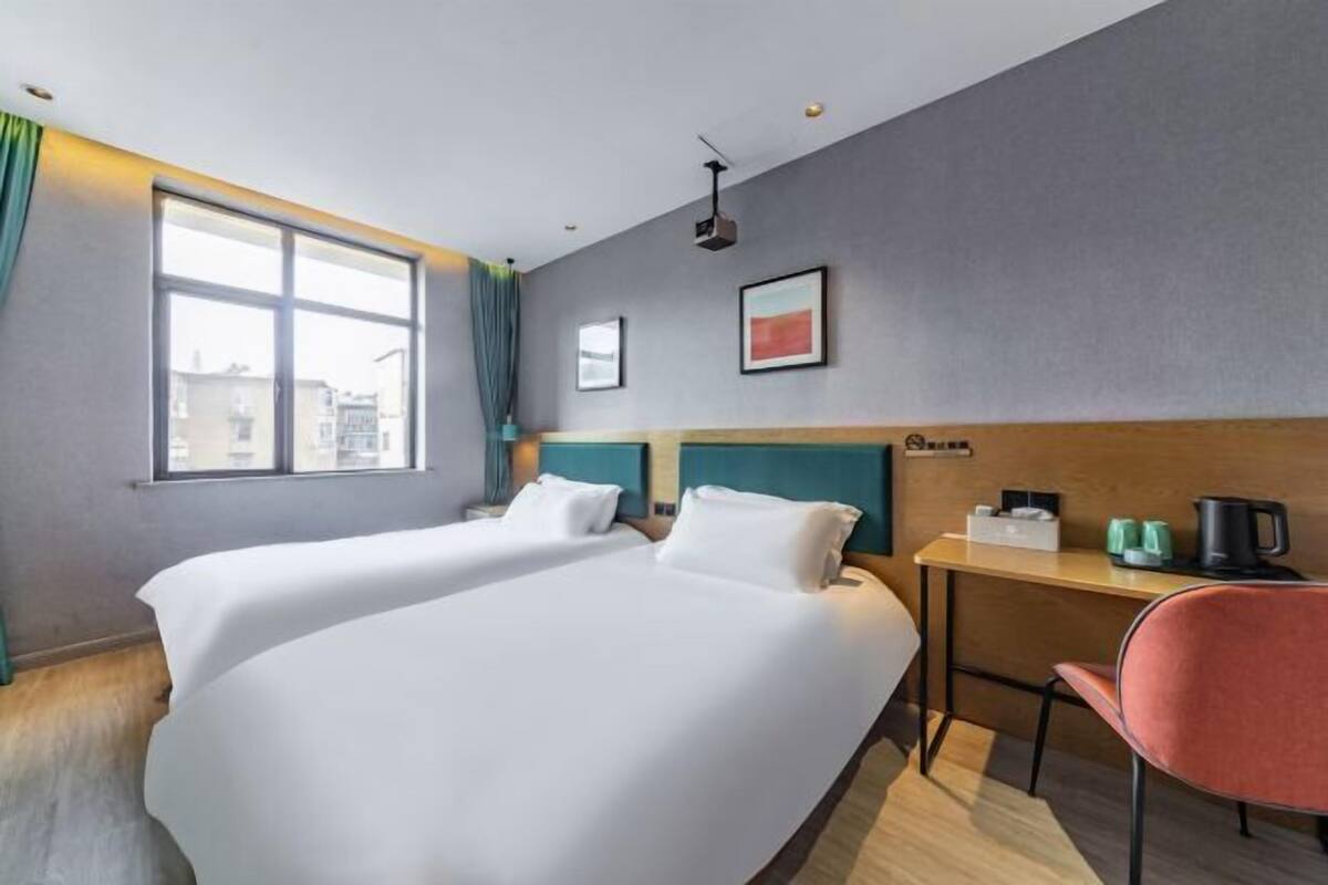 Een hotelkamer met twee bedden, een bureau, een stoel, een raam en een projector.