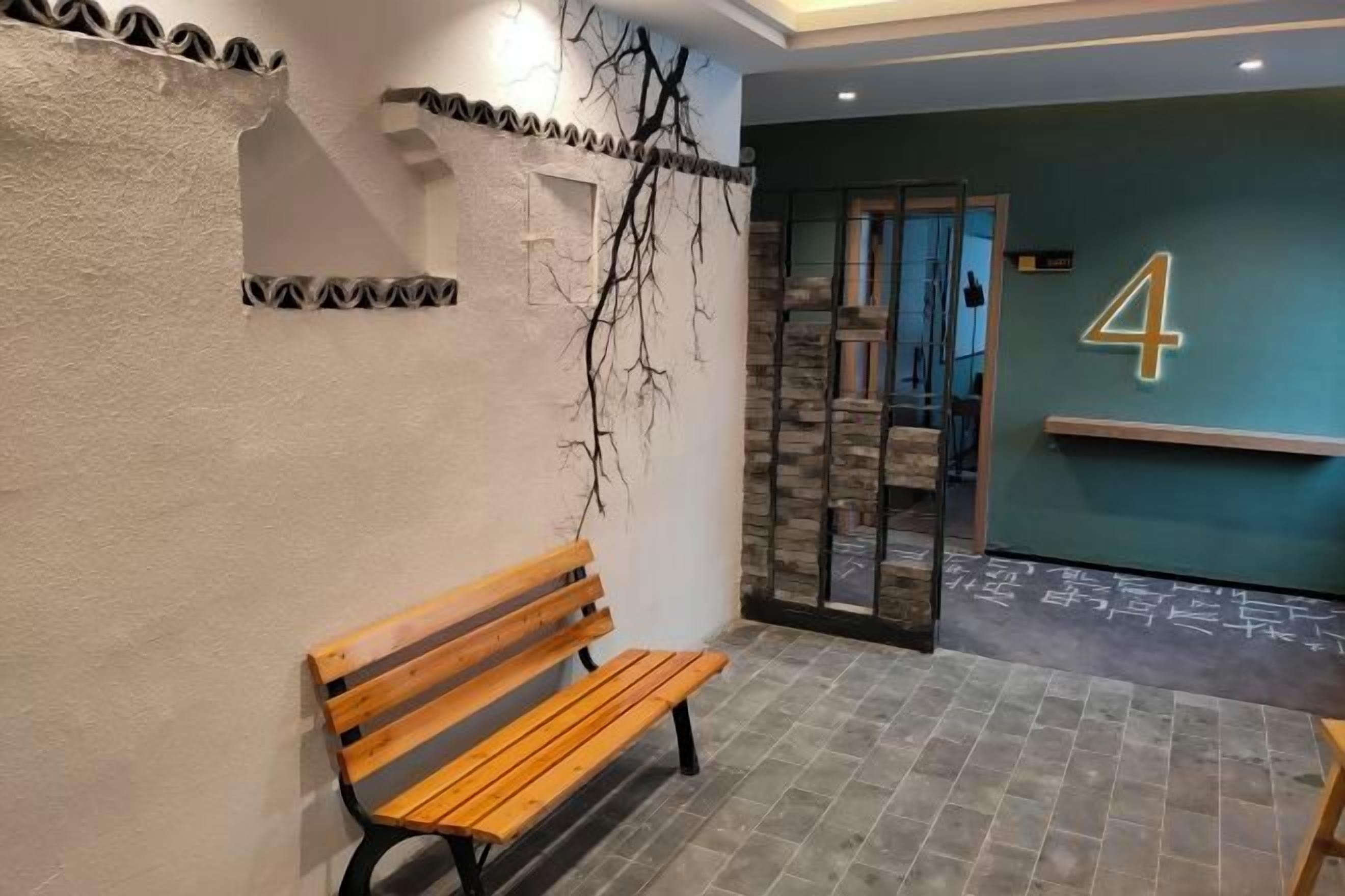 A bench in a hallway with a wall-mounted number sign, a textured wall, and a door leading to another room.