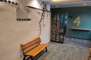 Een bank in een gang met een wandbevestigd nummerbord, een gestructureerde muur en een deur naar een andere kamer.