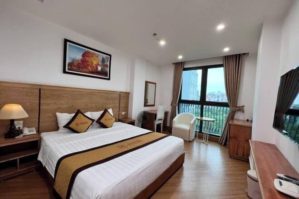 A hotel room with a large bed, a desk, a chair, and a balcony with a view.