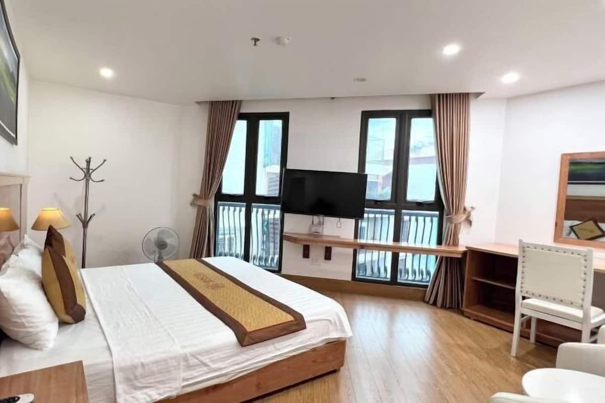 A hotel room with a bed, a desk, a TV, and a balcony with curtains.