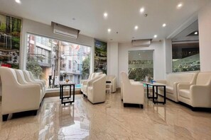 Un hall de hotel con áreas de descanso, una mesa de recepción y grandes ventanales que ofrecen vistas al exterior.