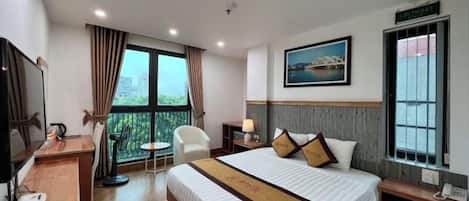 A hotel room with a bed, a desk, a chair, a TV, and a window with a view.