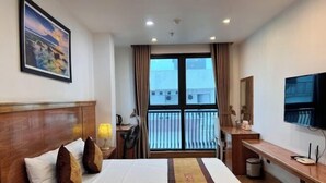 A hotel room with a bed, a desk, a chair, a TV, and a window with curtains. - Kezan Hotel 4m2 (Vo Cuong)