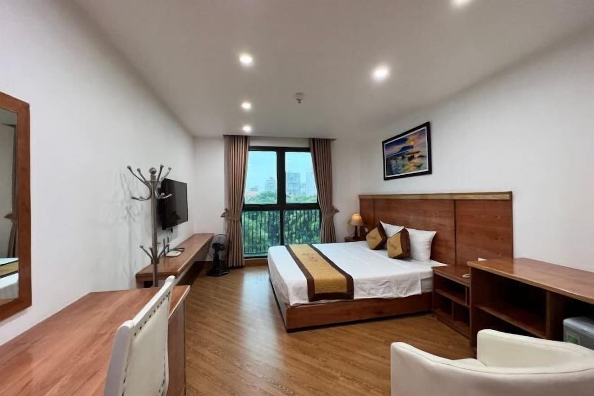A hotel room with a wooden bed, a desk, a chair, a TV, and a window with curtains.