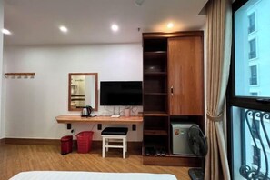 A hotel room with a wooden desk, a TV, a wardrobe, a bed, and a window with curtains. - Kezan Hotel 4m2 (Vo Cuong)