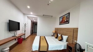 A hotel room with a bed, a TV, a wooden headboard, a nightstand, a lamp, and a painting on the wall. - Kezan Hotel 4m2 (Vo Cuong)