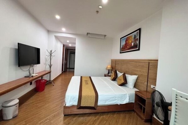 A hotel room with a bed, a TV, a wooden headboard, a nightstand, a lamp, and a painting on the wall. - Kezan Hotel 4m2 (Vo Cuong)