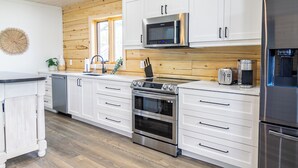 A modern kitchen with white cabinets, stainless steel appliances, and a wooden ceiling. - Riverside Cabin 5
Three season Riverside escape (Campbellford)