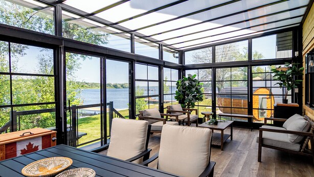 A spacious conservatory with large windows overlooking a lake, furnished with chairs and a table. - Riverside Cabin 5
Three season Riverside escape (Campbellford)