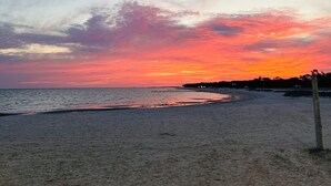 Ein Strand mit Sonnenuntergangshimmel, sandigem Ufer und einem Holzpfosten.