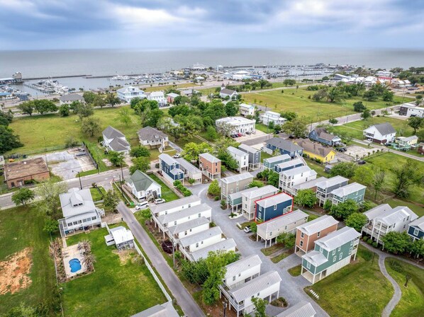An aerial view of a coastal residential area with houses, a marina, and a large body of water in the background.