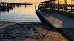 Eine Uferpromenade mit einer Anlegestelle, die in ruhiges Wasser führt, bewölkter Himmel und Sonnenuntergang.