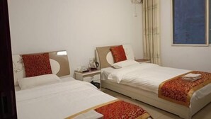 A hotel room with two single beds, a small bedside table with a lamp, an air conditioning unit, and a window with curtains.