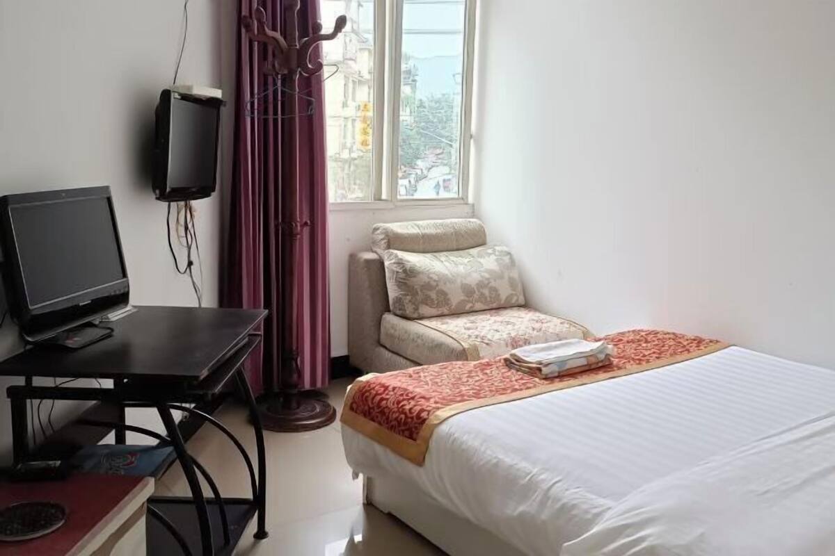 Ein Hotelzimmer mit einem Bett, einem Schreibtisch mit Computer, einem Fernseher und einem Fenster mit Vorhängen.