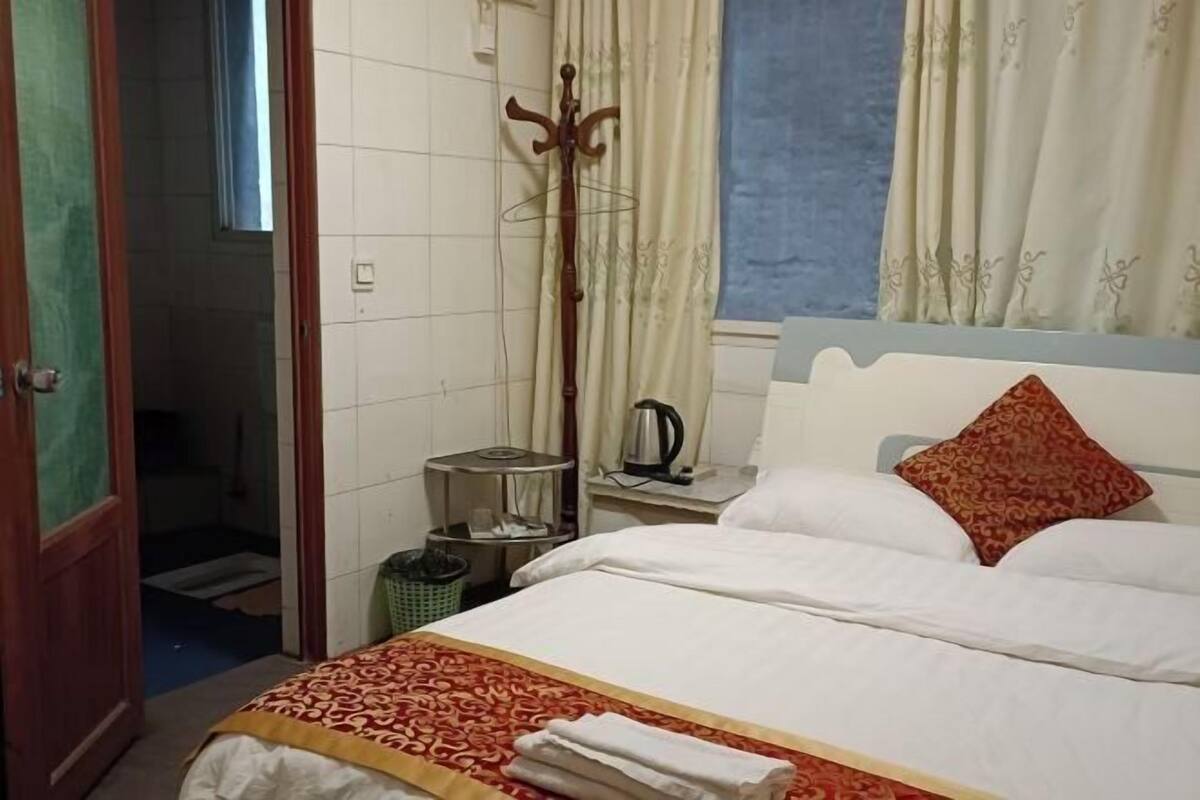 Ein Hotelzimmer mit einem Bett, einem Holzmantelständer, einem Wasserkocher und einem Fenster mit Vorhängen.