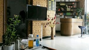 A hotel reception area with a flat-screen TV, a reception desk, a potted plant, and a seating area.