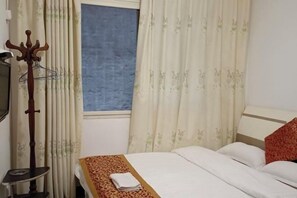 A hotel room with a bed, a wooden coat rack, and a window with curtains. - yaan jinsanjiao hotel (Ya'an)