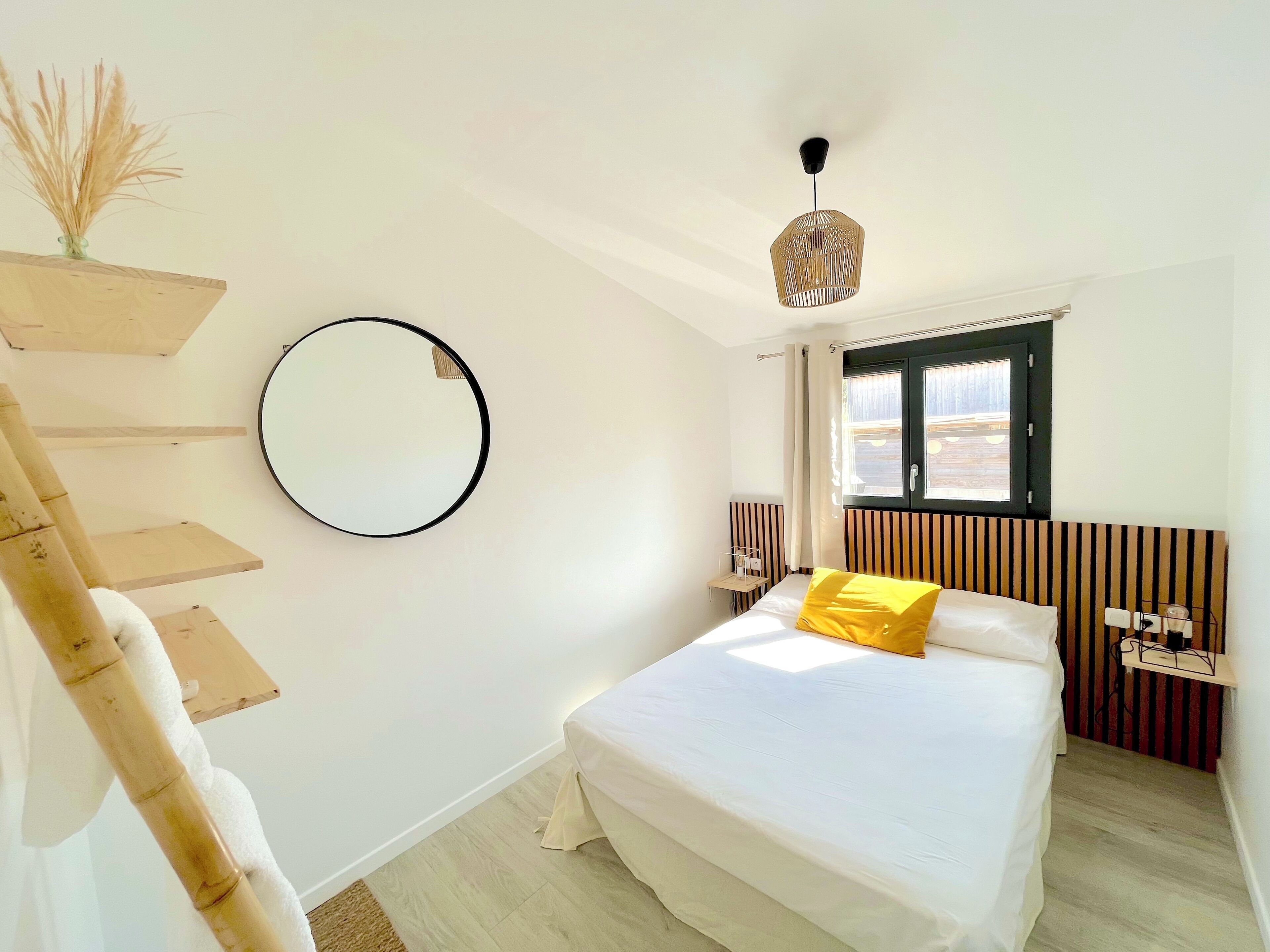 A bedroom with a bed, a round mirror, a hanging light fixture, and a window with curtains.