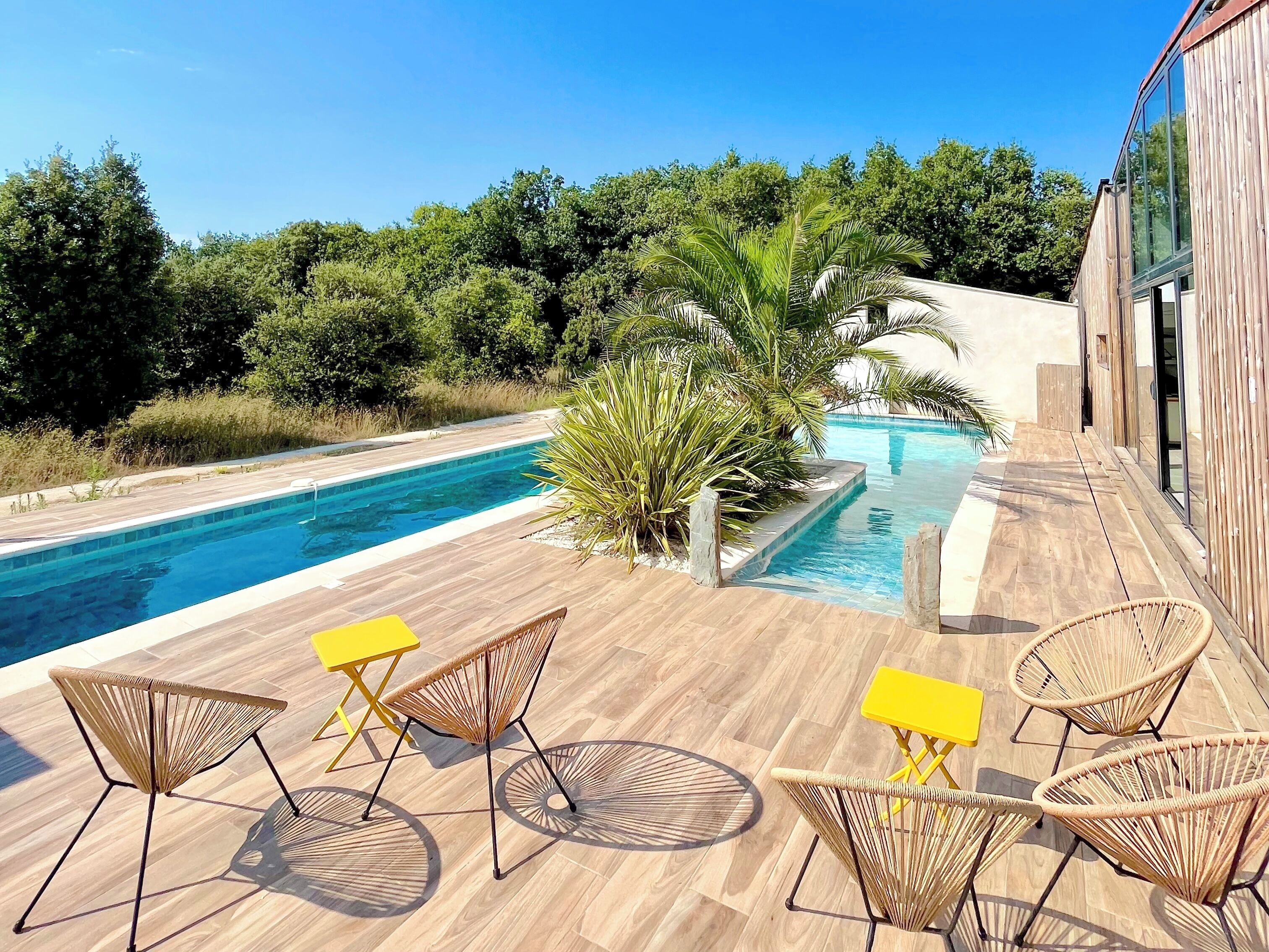 Un área junto a la piscina con una terraza de madera, sillas de descanso y una pequeña mesa.