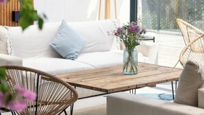 Een moderne woonkamer met een witte bank, een houten salontafel en rieten stoelen.