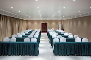 A conference room with rows of tables, white chairs, and a curtain backdrop.