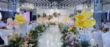 A banquet hall with a central aisle flanked by floral arrangements and white chairs.