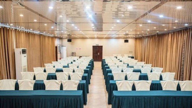 A conference room with rows of tables and chairs, a wooden panel wall, and a door at the far end. - Jialong Hotel (Guangyuan High-speed Railway Station) (Guangyuan)