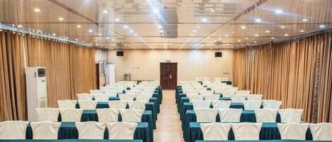 A conference room with rows of tables and chairs, a wooden door, and a ceiling with recessed lighting.