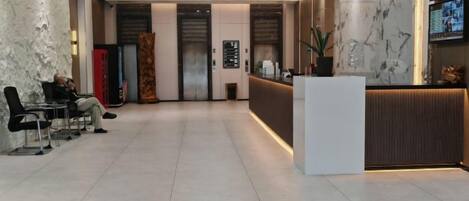 Un hall de hotel con mostrador de recepción, zona de estar y una planta grande.
