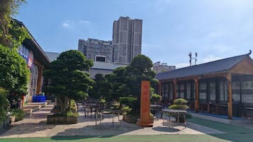 Pátio com um edifício tradicional, um prédio moderno alto ao fundo e céu claro.