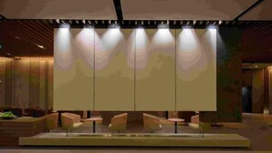 Eine moderne Lobby mit einer zentralen Sitzecke, einem großen, beleuchteten Bildschirm und einem Holzbüro.