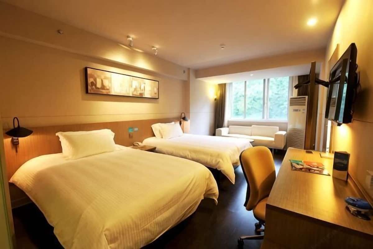 Hotellihuone, jossa on kaksi sänkyä, työpöytä, tuoli, televisio ja ikkuna.