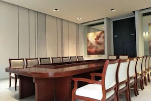 A conference room with a long table and chairs, a large abstract painting on the wall, and a dark door in the background. - Jinjiang Inn Select (Lushan City)