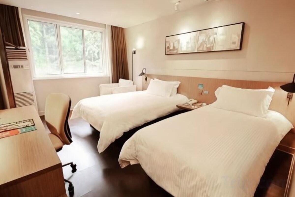 A hotel room with two beds, a desk, a chair, and a window with curtains.