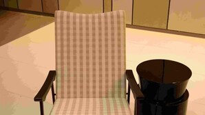 Un sillón a cuadros con respaldo alto y un objeto cilíndrico negro a su lado.