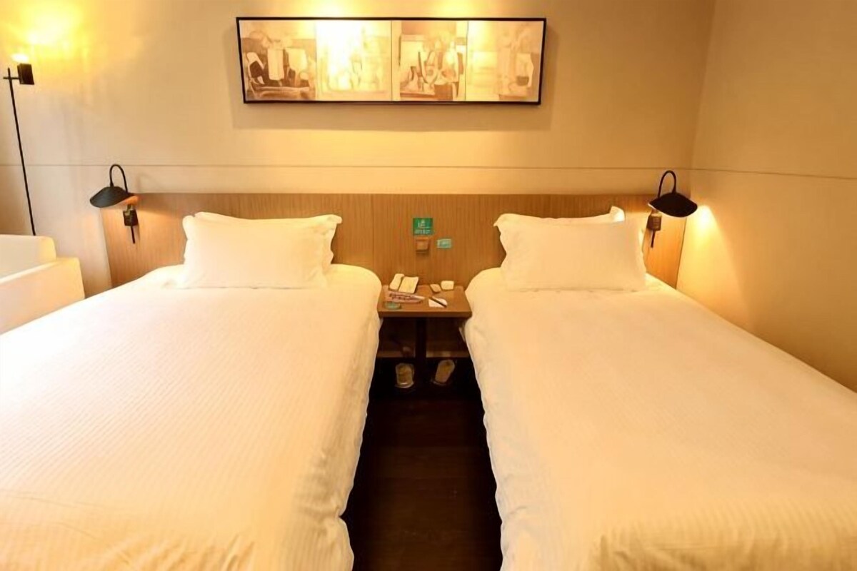 A hotel room with two beds, a nightstand, a wall-mounted phone, and a painting above the beds.