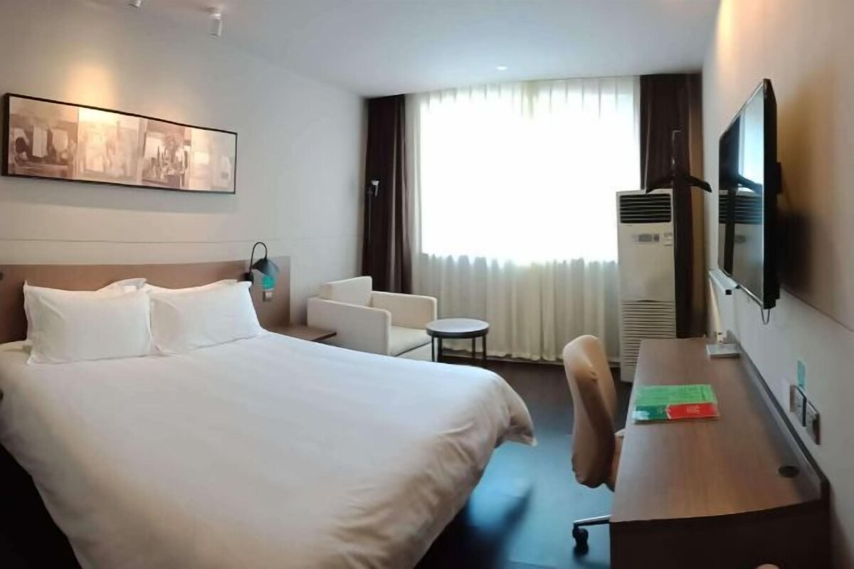 A hotel room with a large bed, a desk, a chair, a television, and a window with curtains.
