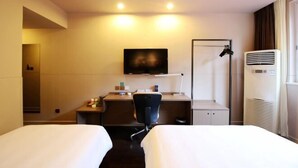 Habitación de hotel con dos camas, un escritorio con silla, un televisor montado en la pared y un equipo de aire acondicionado.