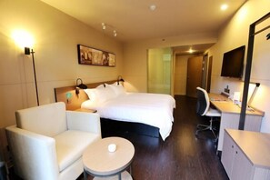 A hotel room with a bed, a desk, a chair, a small round table, and a wall-mounted TV. - Jinjiang Inn Select (Lushan City)