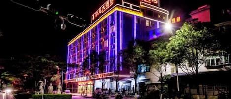 Un hotel de varios pisos con señalización iluminada, un área de entrada bien cuidada y un patio amurallado.